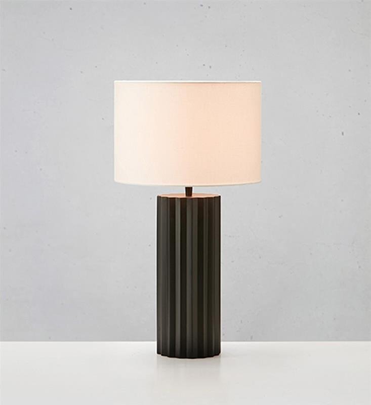 Lampa stołowa z cylindrycznym, żebrowanym czarnym korpusem i białym abażurem, ustawiona na jasnym tle.