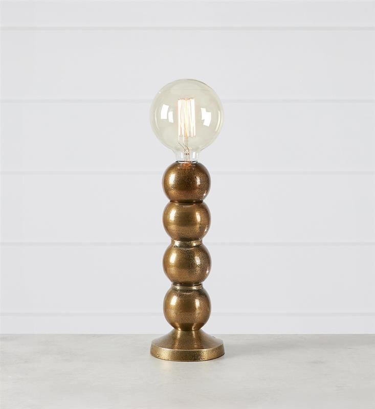 Stylowa lampa stołowa z metalową podstawą w kształcie kul i przezroczystą żarówką na górze, ustawiona na jasnym tle.