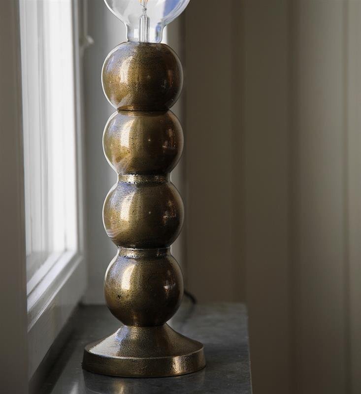 Lampa stołowa z metalową podstawą o kulistym kształcie, ustawiona na parapecie przy oknie.