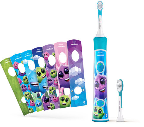 Na obrazie widoczna jest szczoteczka soniczna z kolorowymi nakładkami z postaciami przypominającymi potworki. Obok szczoteczki znajduje się dodatkowa końcówka.