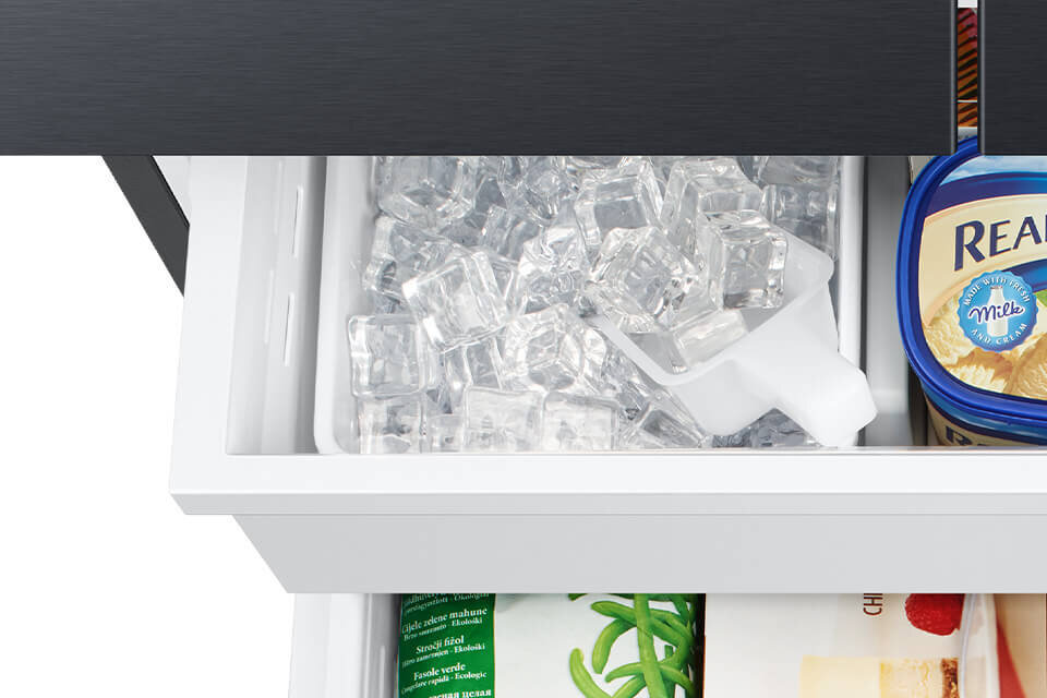 Otwarta szuflada lodówki z kostkami lodu i białą łopatką. Obok znajduje się opakowanie lodów z napisem \'Real\'.