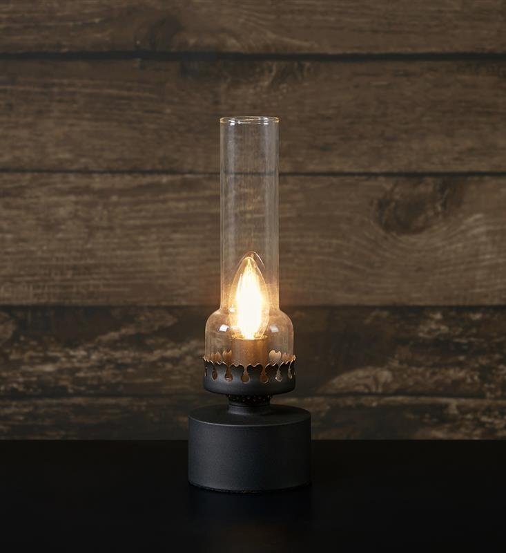 Stylowa lampa stołowa z przezroczystym kloszem i świecącą żarówką, ustawiona na ciemnym tle z drewnianą teksturą.