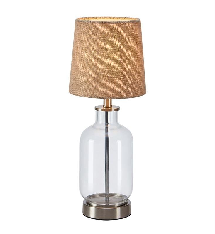 Lampa stołowa z przezroczystą szklaną podstawą i beżowym abażurem, umieszczona na neutralnym białym tle.