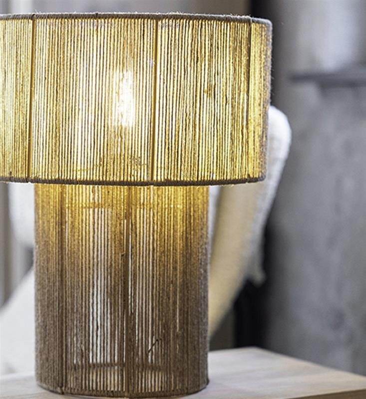 Lampa stołowa z abażurem wykonanym z pionowych, cienkich prętów, emitująca ciepłe światło. Stoi na drewnianym stoliku w jasnym wnętrzu.