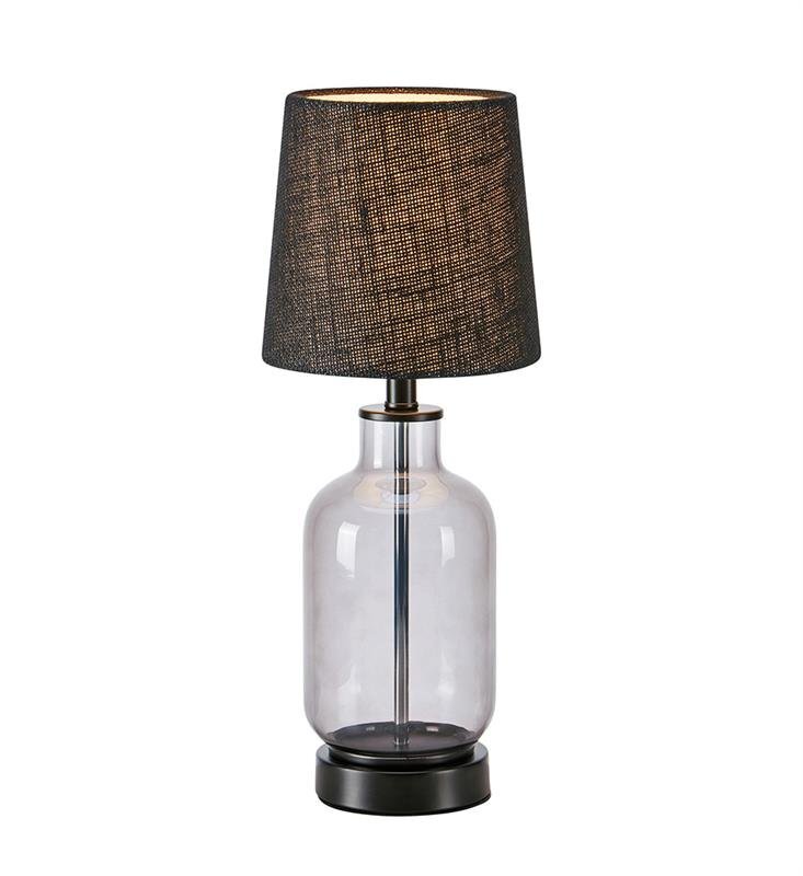 Lampa stołowa z przezroczystą szklaną podstawą i ciemnym abażurem o teksturowanej powierzchni, ustawiona na neutralnym tle.