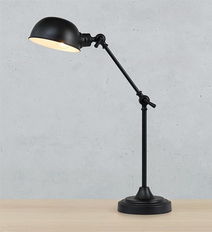Czarna lampa biurkowa na wysięgniku z okrągłym kloszem, umieszczona na drewnianym blacie. Tło jest szare i jednolite.