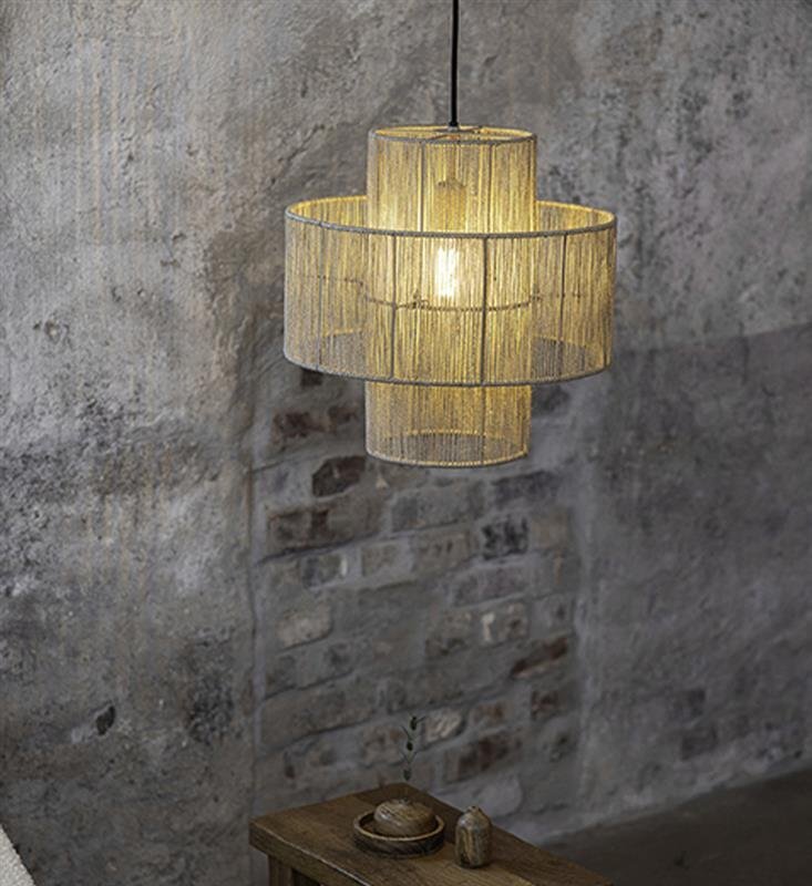 Lampa wisząca złożona z trzech cylindrycznych abażurów wykonanych z jasnego materiału, zawieszona na tle szarej, ceglanej ściany. Pod lampą znajduje się drewniany stolik z dekoracyjnymi przedmiotami.