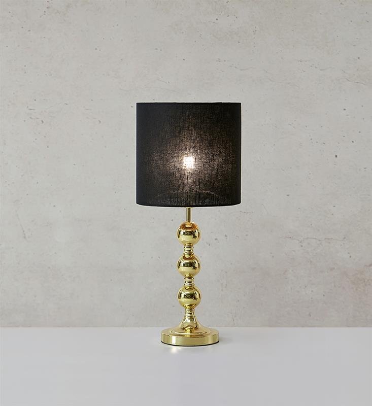 Lampa stołowa z czarnym abażurem i złotą, kulistą podstawą na tle jasnej ściany.