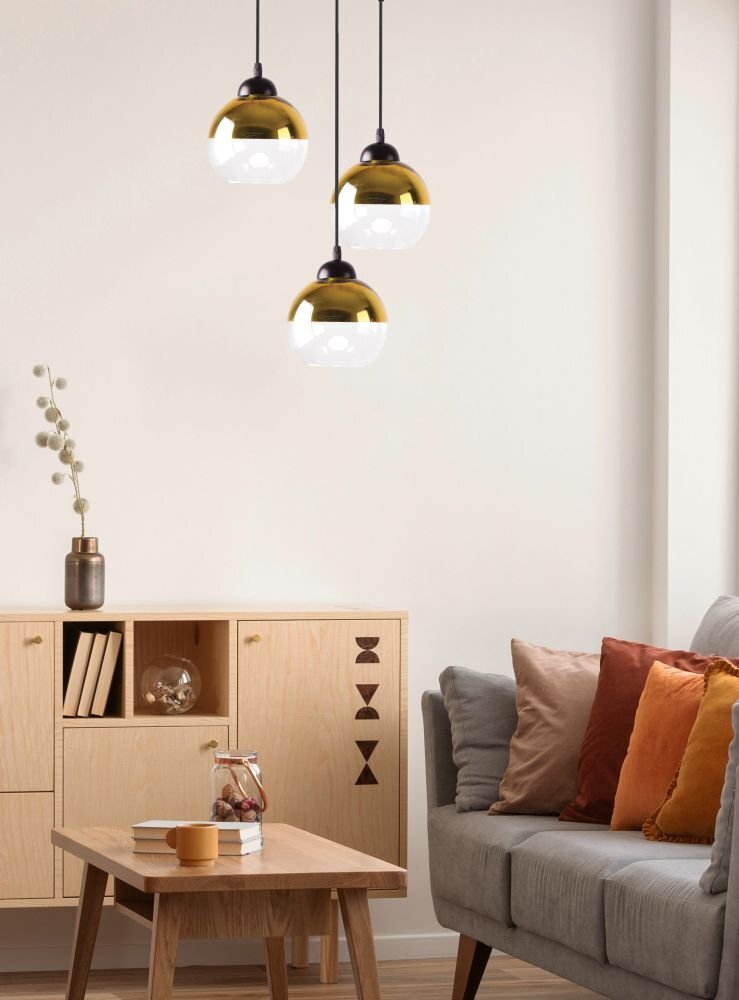 Wnętrze pokoju z trzema wiszącymi lampami o złotych kloszach. W tle znajduje się drewniana komoda z dekoracjami i szara sofa z kolorowymi poduszkami.