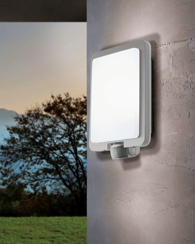 Lampa ścienna z białym kloszem zamontowana na zewnętrznej ścianie budynku, w tle widoczny krajobraz z drzewami i górami.
