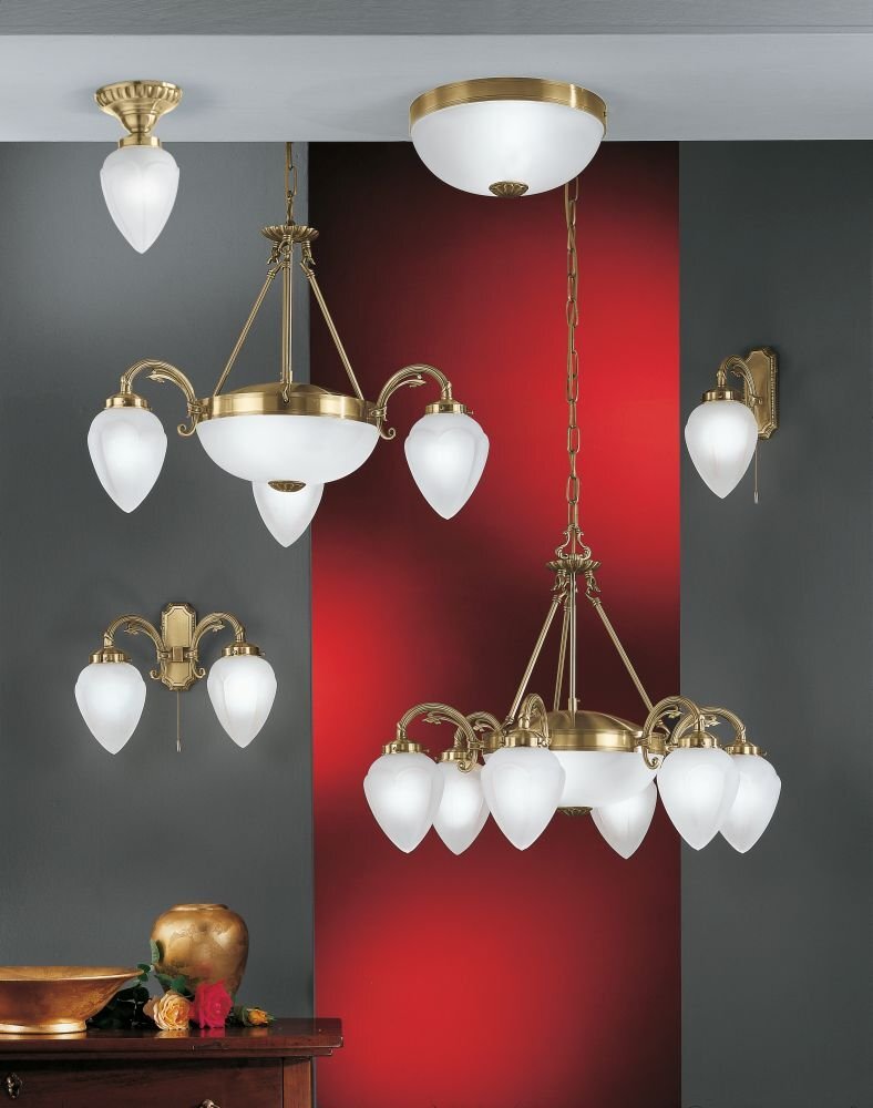 Na obrazie widoczne są różne modele klasycznych lamp sufitowych i ściennych z białymi, satynowanymi kloszami i elementami w kolorze patyny. Tło jest w odcieniach szarości i czerwieni, a na pierwszym planie znajduje się drewniany stół z dekoracjami.
