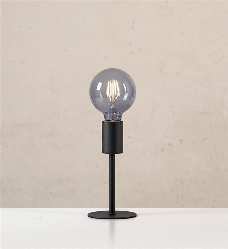 Czarna lampa stołowa z okrągłą żarówką na tle jasnej ściany.