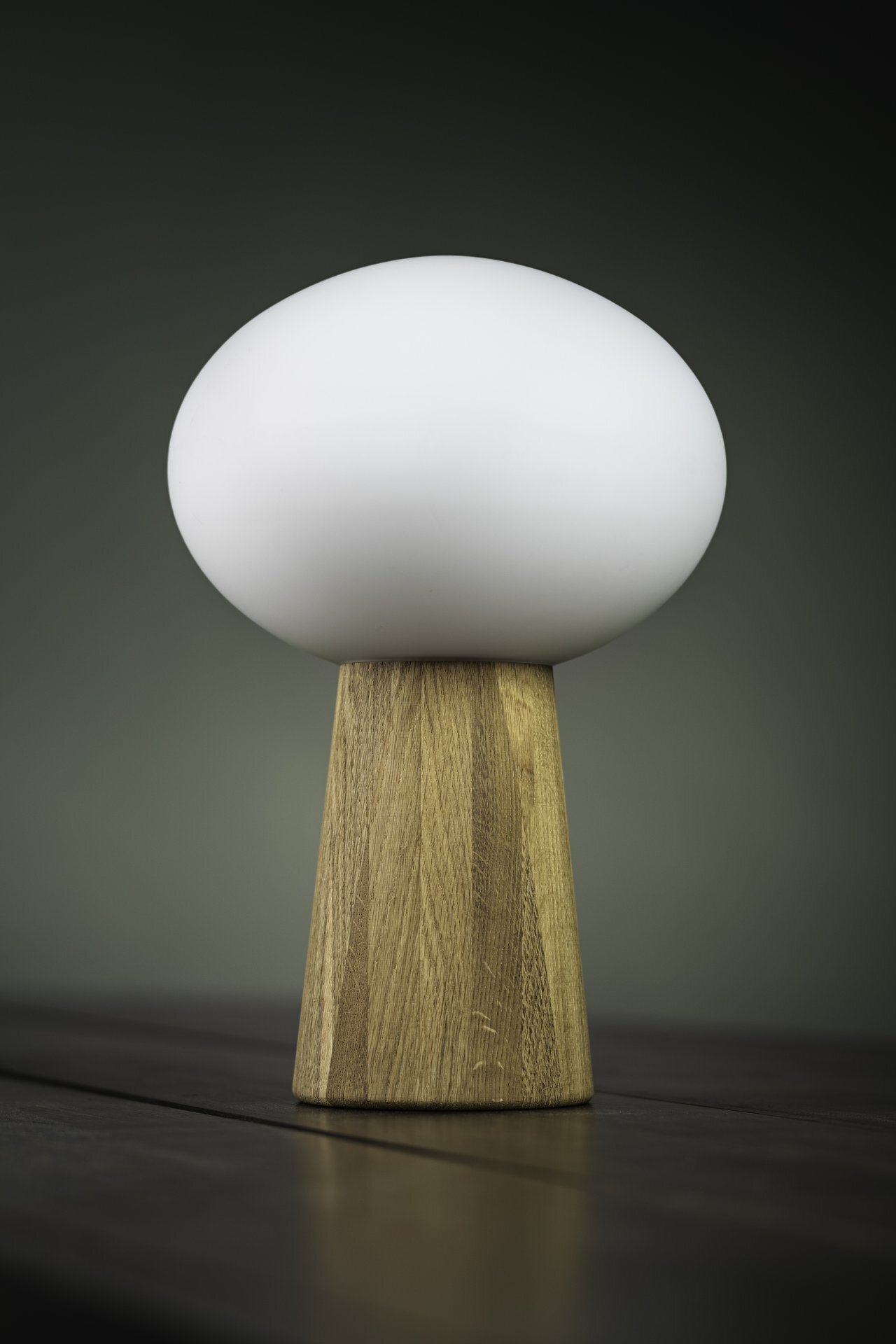 Lampa stołowa z białym, kulistym kloszem i drewnianą podstawą, ustawiona na ciemnym stole z neutralnym tłem.
