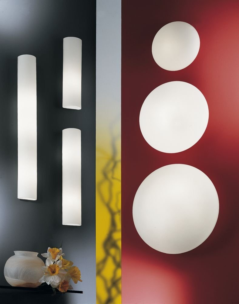 Obraz przedstawia dwie grupy lamp ściennych na tle ciemnej i czerwonej ściany. Po lewej stronie znajdują się trzy podłużne lampy, a po prawej trzy okrągłe lampy.