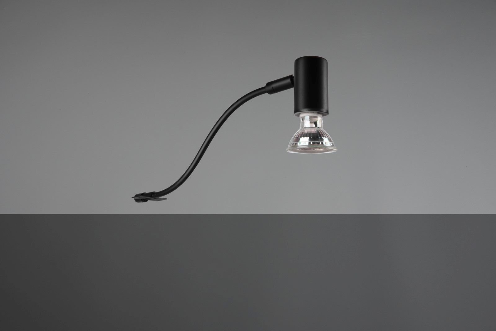 Czarna lampa z przezroczystym kloszem na tle szarej ściany.