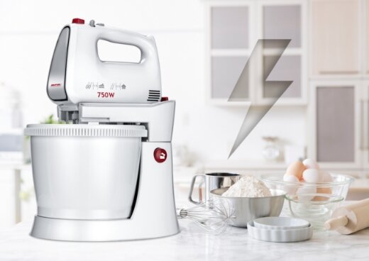 Biały mikser z misą o mocy 750W, z widocznym logo \'MPM\', stoi na blacie kuchennym. Obok znajdują się składniki do pieczenia, takie jak mąka, jajka i wałek do ciasta.