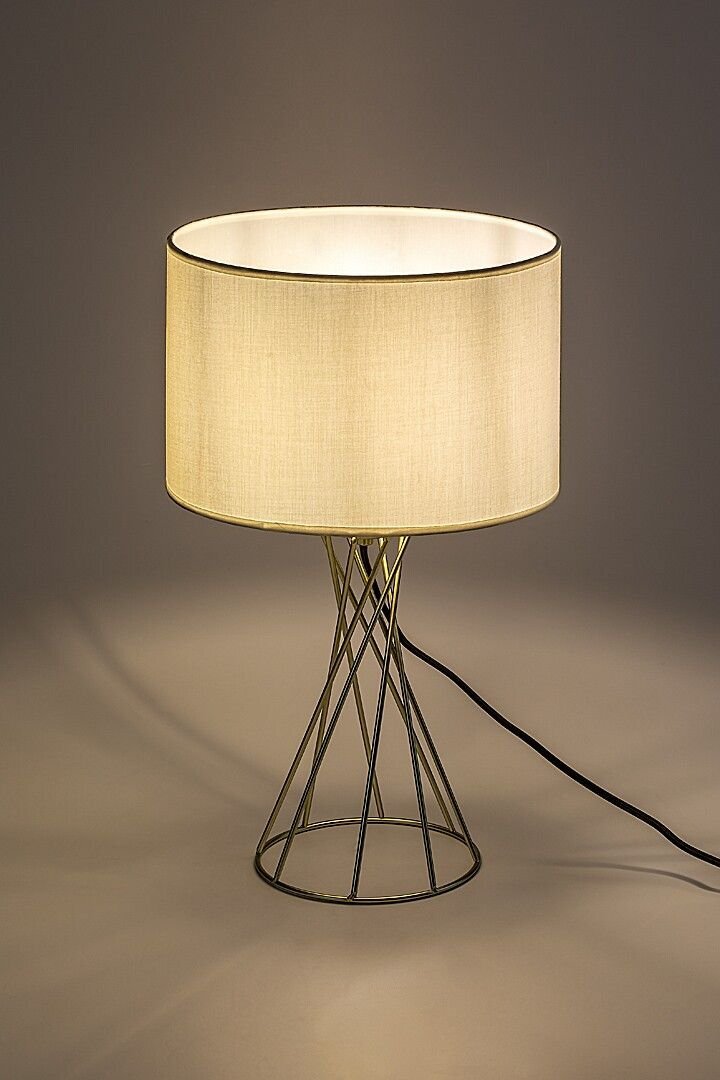 Lampa stołowa z metalową podstawą o geometrycznym wzorze i jasnym abażurem, stojąca na neutralnym tle.