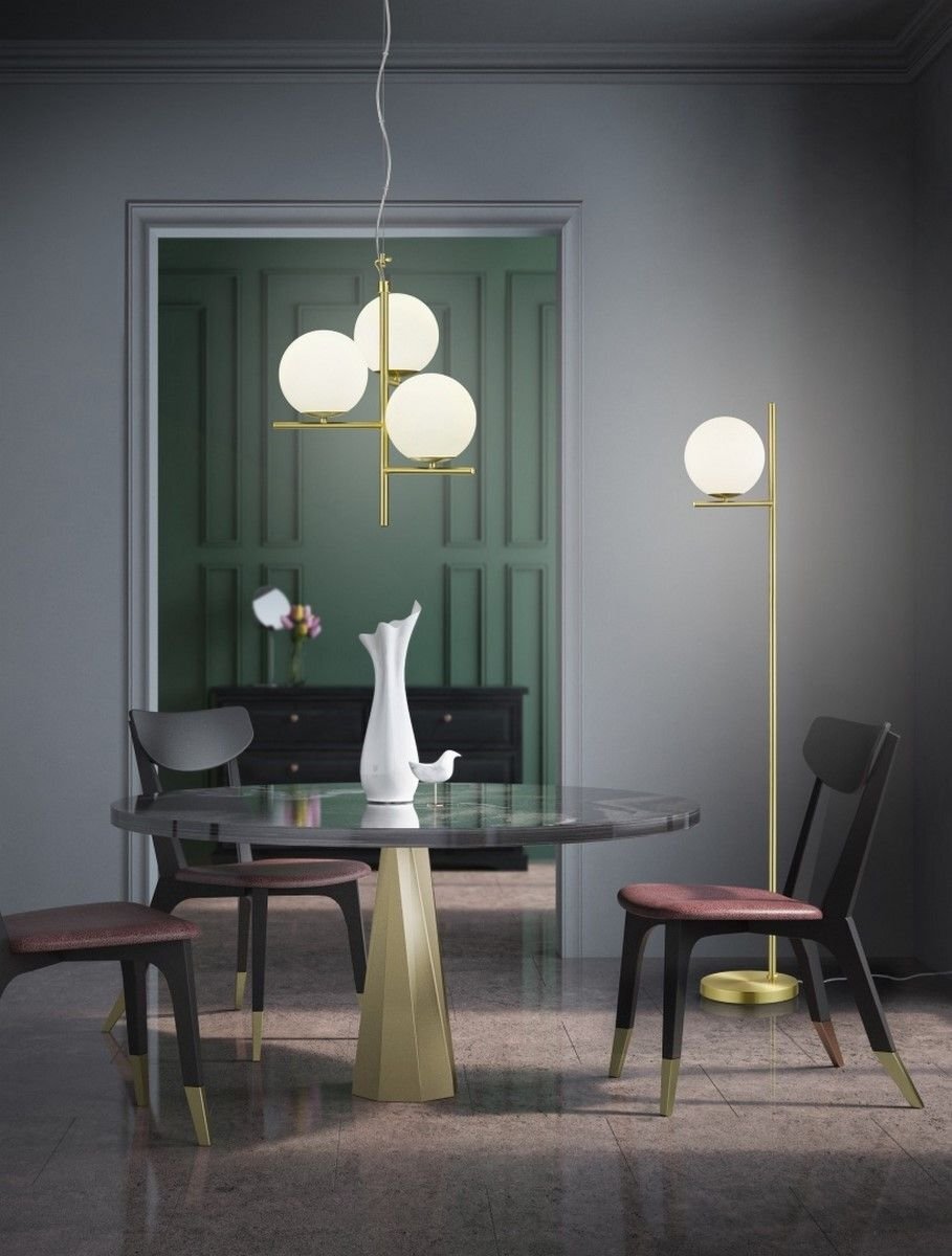 Elegancka lampa sufitowa z trzema kulistymi kloszami wisi nad okrągłym stołem z wazonem, otoczonym krzesłami w nowoczesnym wnętrzu.