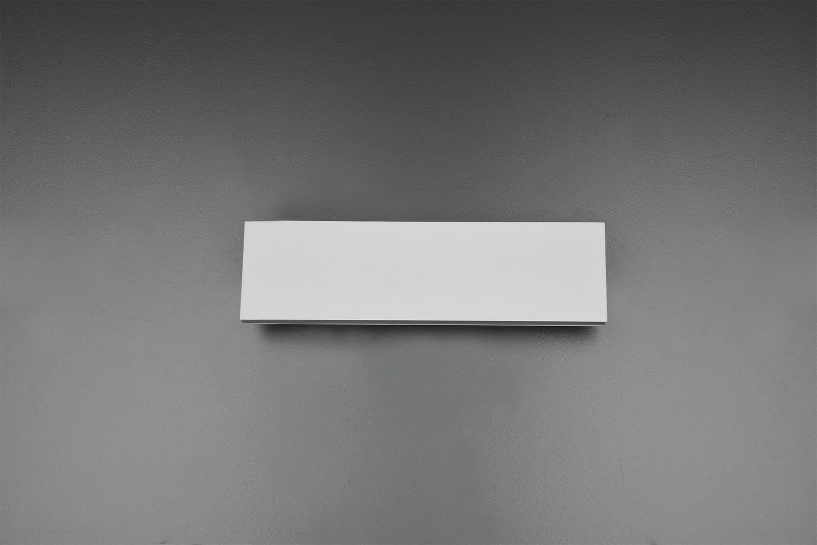 Prostokątny, biały kinkiet zamontowany na szarej ścianie. Lampa ma nowoczesny, minimalistyczny design.