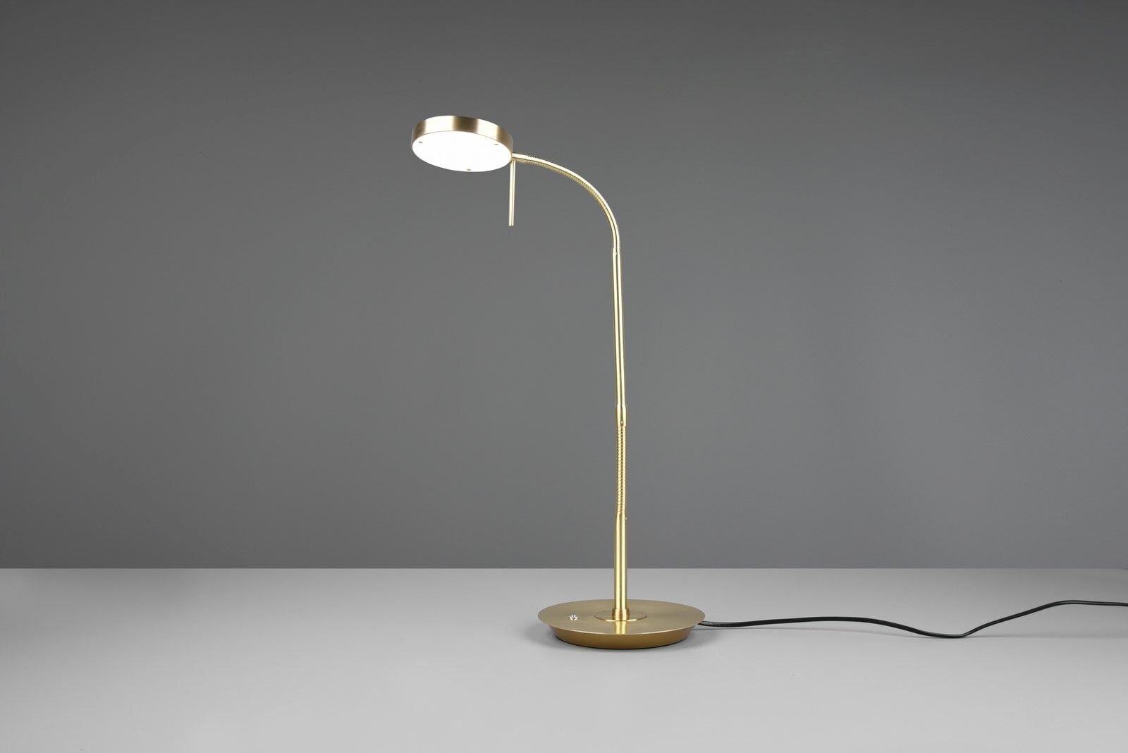 Złota lampa biurkowa LED z okrągłym kloszem na szarej powierzchni, z widocznym czarnym kablem zasilającym.