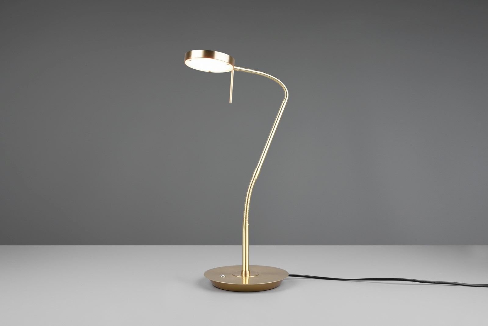 Złota lampa biurkowa LED o nowoczesnym designie, stojąca na szarej powierzchni z ciemnym tłem.