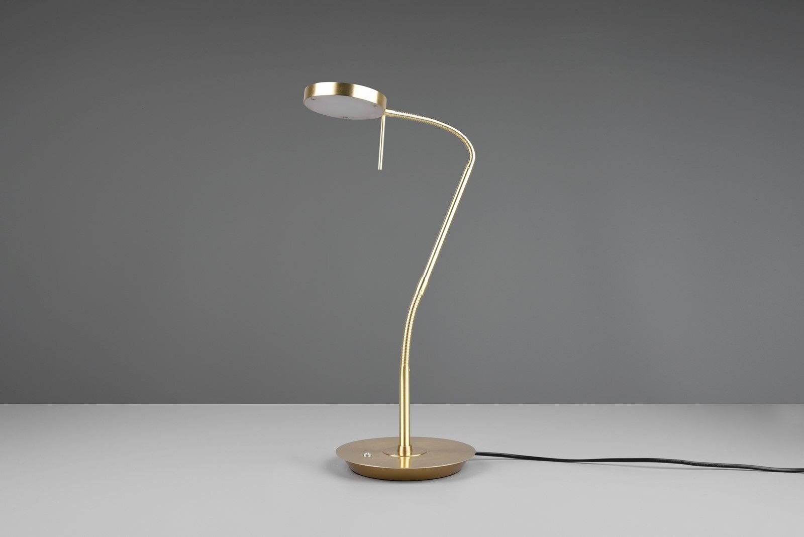Złota lampa biurkowa LED o nowoczesnym designie, stojąca na szarej powierzchni z widocznym czarnym kablem zasilającym.