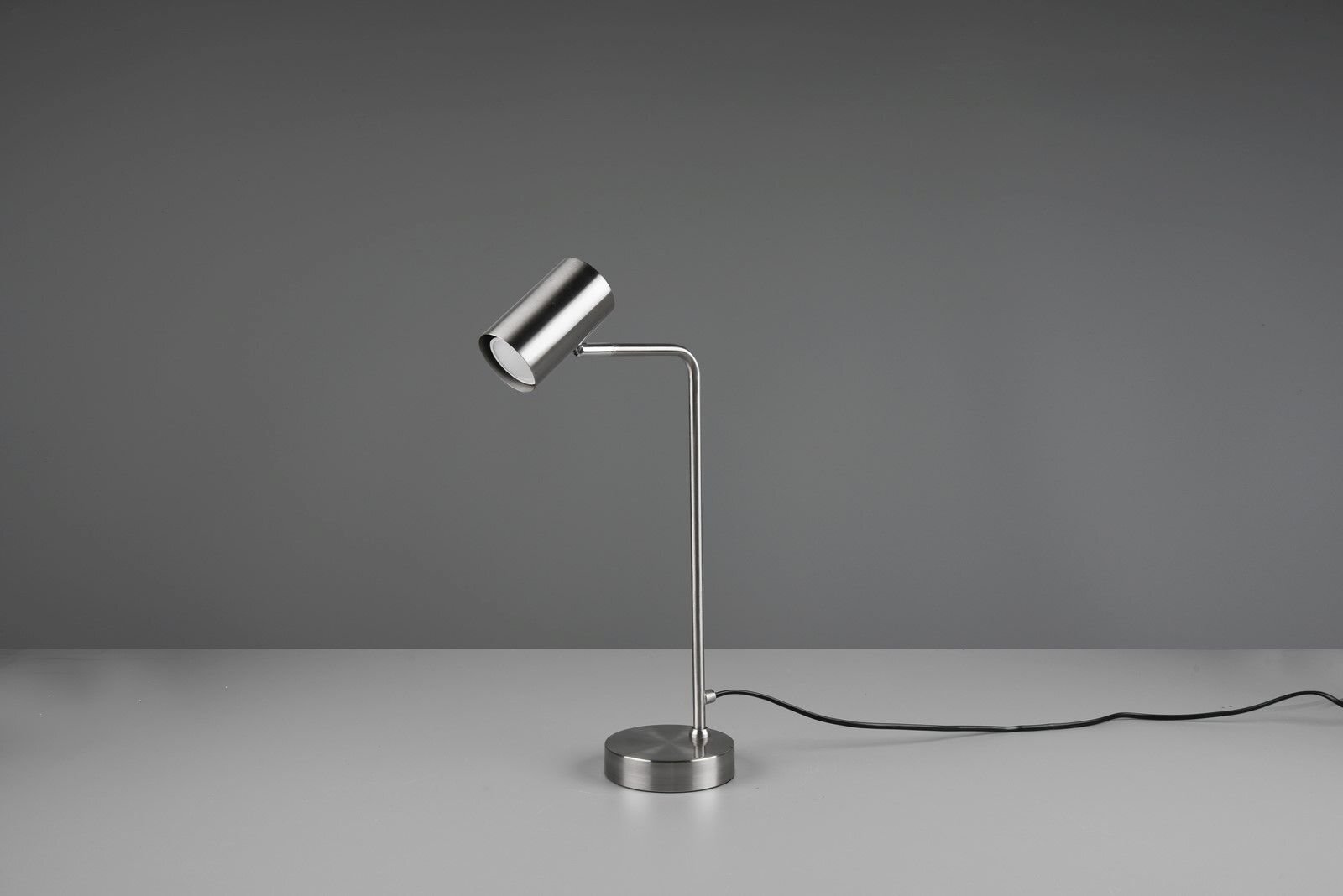 Srebrna lampa biurkowa o nowoczesnym designie z cylindrycznym kloszem i prostym ramieniem na szarej powierzchni.