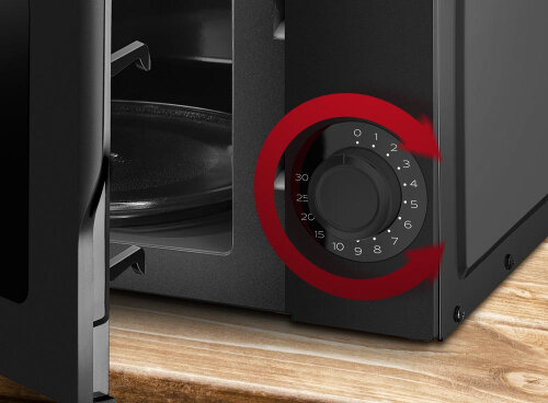 Zdjęcie przedstawia otwartą kuchenkę mikrofalową z widocznym pokrętłem do regulacji czasu, oznaczonym cyframi od 0 do 30. Na pokrętle znajduje się czerwona strzałka wskazująca kierunek obrotu.