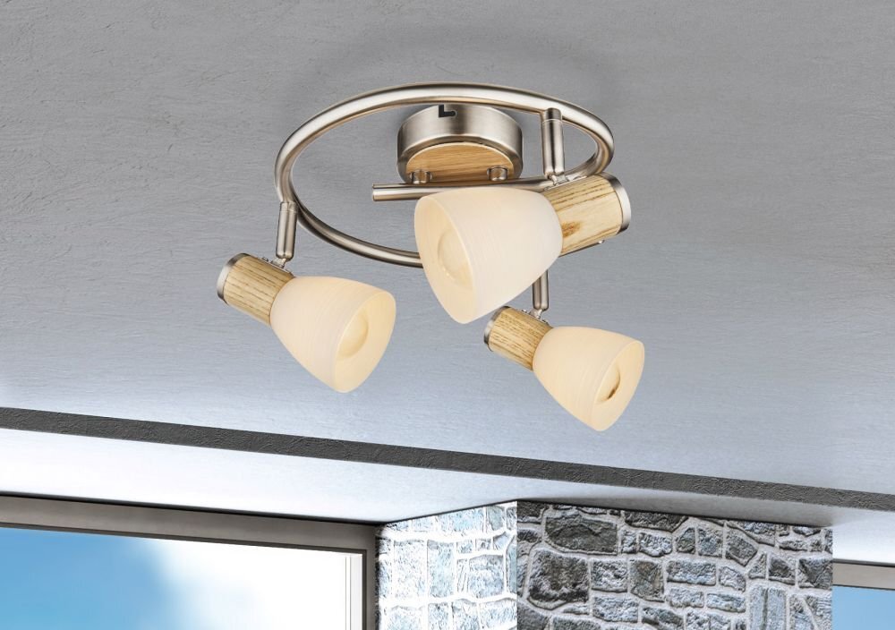 Lampa sufitowa z trzema kloszami w kolorze opalowym, zamontowana na metalowej konstrukcji w kolorze niklu z elementami drewnianymi. W tle widoczny jest fragment ściany z kamienia i okno.