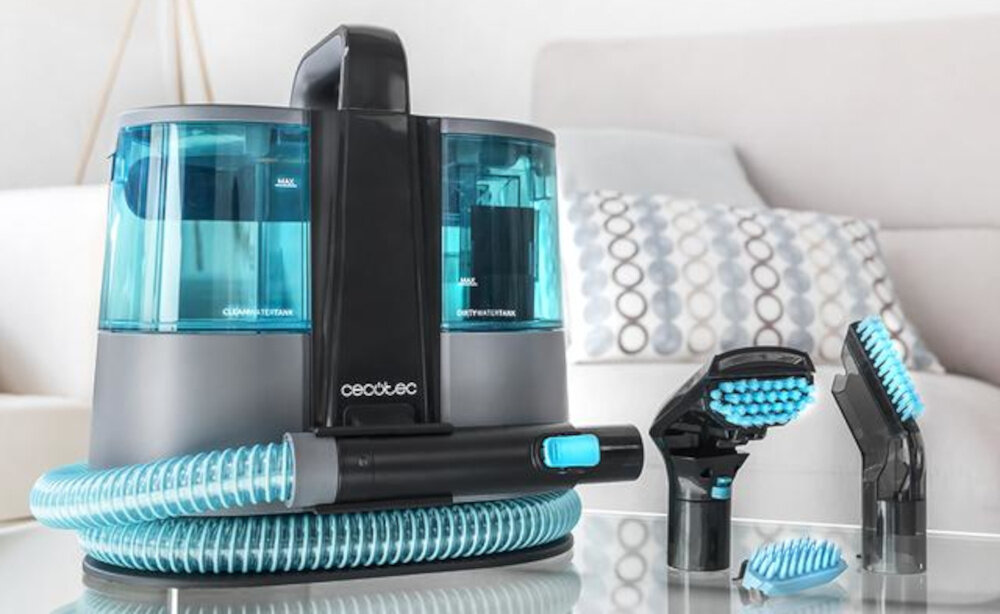 Na obrazie widoczny jest odkurzacz piorący z przezroczystymi, niebieskimi zbiornikami oraz elastycznym wężem. Obok znajdują się trzy różne końcówki czyszczące, a na urządzeniu widnieje logo \'cecotec\'.