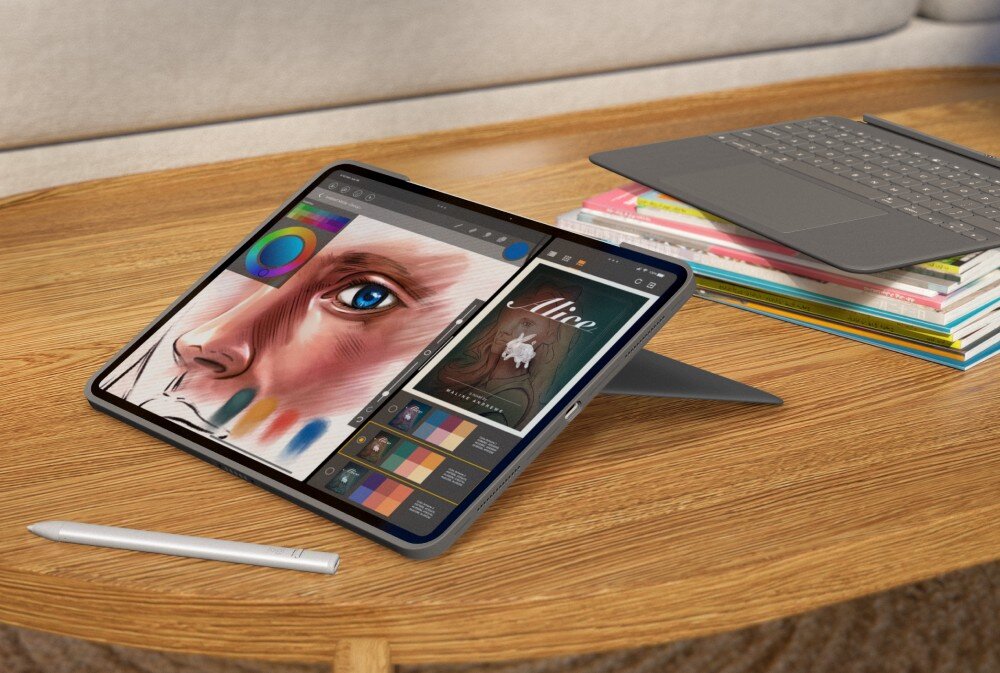 Na drewnianym stole znajduje się tablet z wyświetlonym rysunkiem twarzy i paletą kolorów, obok leży rysik. W tle widać klawiaturę na stosie książek.