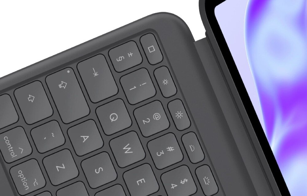 Zbliżenie na grafitową klawiaturę z widocznymi klawiszami, takimi jak Q, W, E, R, A, S, D, F oraz symbolami specjalnymi. Obok klawiatury znajduje się fragment ekranu z fioletowym wzorem.