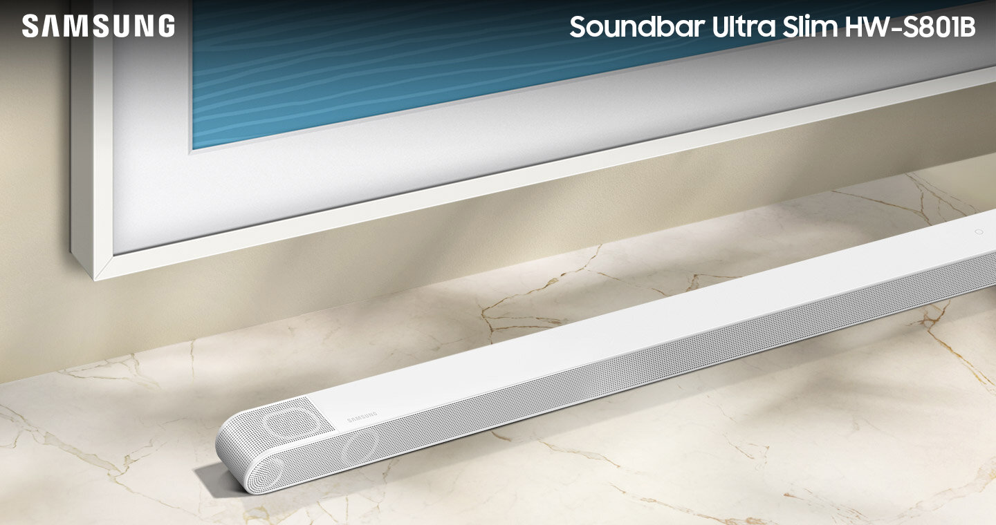 Biały soundbar o smukłej konstrukcji umieszczony na marmurowej powierzchni przed telewizorem. Widoczne logo \'SAMSUNG\' oraz napis \'Soundbar Ultra Slim HW-S801B\'.