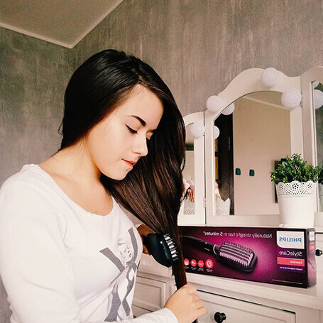 Osoba używa szczotki prostującej do włosów, obok znajduje się pudełko z napisem \'PHILIPS StyleCare\'.