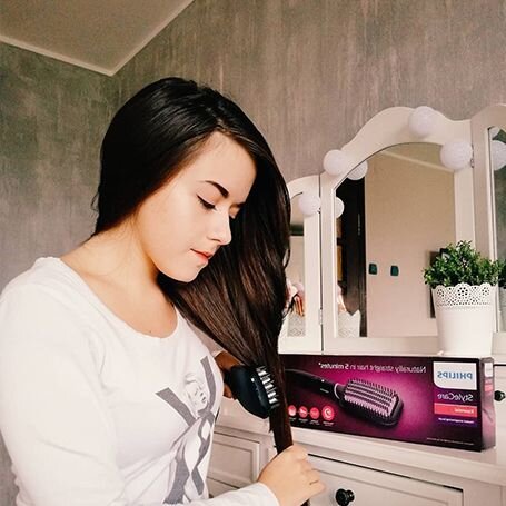 Osoba używa szczotki prostującej do włosów, obok znajduje się pudełko z napisem \'PHILIPS StyleCare\'.