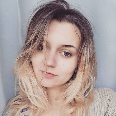 Zdjęcie przedstawia osobę z długimi, falującymi włosami w odcieniach blond i brązu, na tle jasnej zasłony.