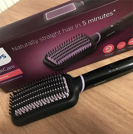 Na drewnianym blacie leży czarna szczotka prostująca z fioletowymi elementami, obok znajduje się pudełko z napisem \'Naturally straight hair in 5 minutes*\'.