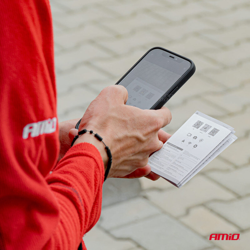 Osoba trzymająca smartfon i instrukcję obsługi z widocznymi kodami QR, ubrana w czerwoną odzież z logo \'AMiO\'. Na dole zdjęcia widoczne jest logo \'AMiO\'.