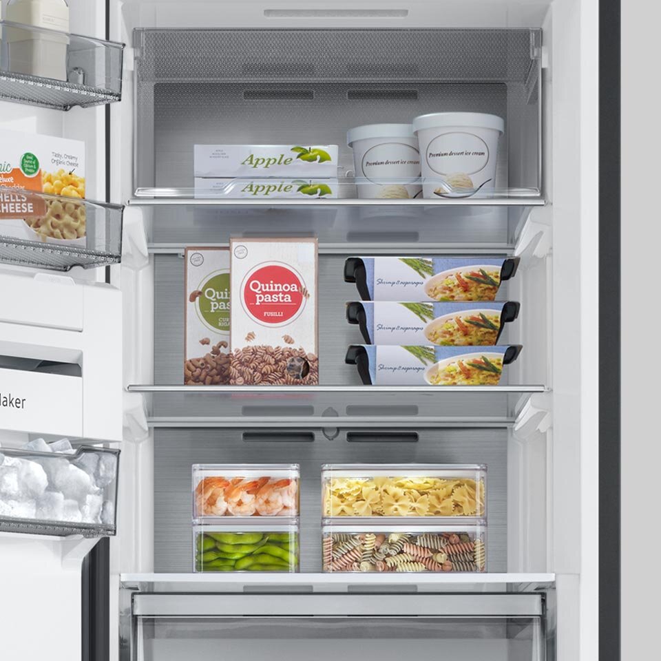 Wnętrze zamrażarki z widocznymi półkami, na których znajdują się różne produkty spożywcze, takie jak opakowania lodów, pudełka z makaronem i mrożonki. Na opakowaniach widoczne są napisy: \'Apple\', \'Quinoa pasta\'.