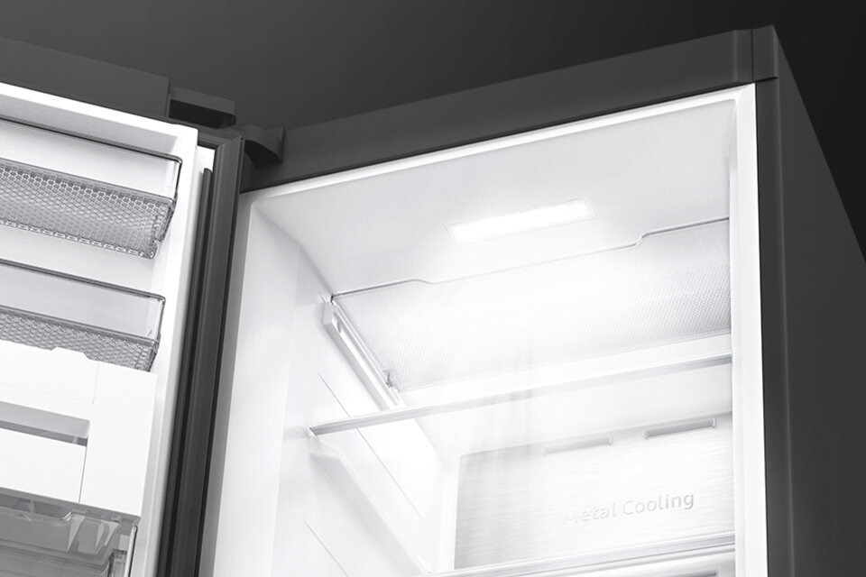 Wnętrze zamrażarki z widocznymi półkami i oświetleniem LED. Na ścianie zamrażarki znajduje się napis \'Metal Cooling\'.