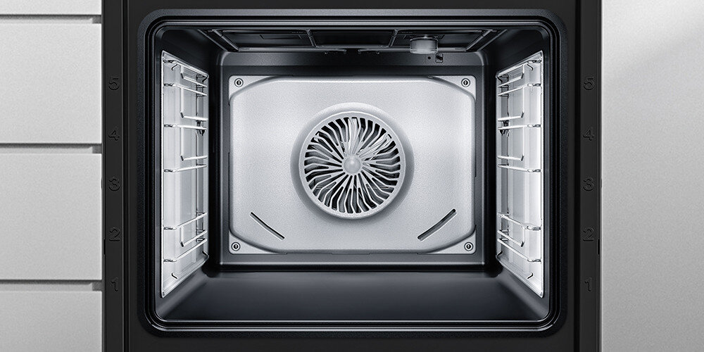 Wnętrze piekarnika z widocznym wentylatorem na tylnej ścianie oraz oznaczeniami poziomów na bocznych ściankach. Piekarnik ma metaliczne wykończenie i prostokątny kształt.