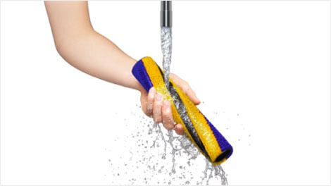 Osoba trzyma żółto-niebieską szczotkę pod strumieniem wody z kranu.