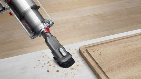 Odkurzacz z wąską końcówką ssącą zbiera okruchy z białej powierzchni obok drewnianej deski.