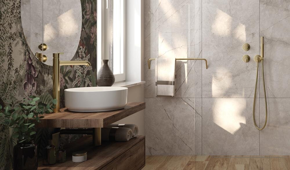 Łazienka z umywalką nablatową na drewnianej półce, obok której znajduje się złota bateria umywalkowa. Ściany wyłożone są jasnymi płytkami, a na jednej z nich wisi ręcznik na złotym uchwycie.