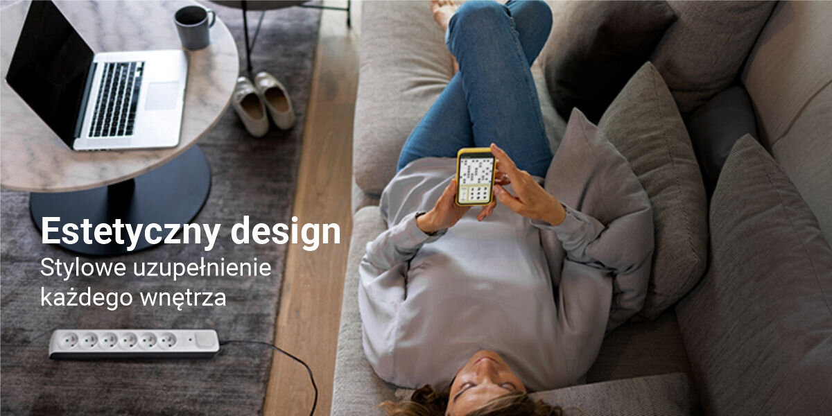 Osoba leży na kanapie, trzymając telefon, obok znajduje się biały przedłużacz z sześcioma gniazdami. Na obrazie widoczny jest tekst: \'Estetyczny design Stylowe uzupełnienie każdego wnętrza\'.