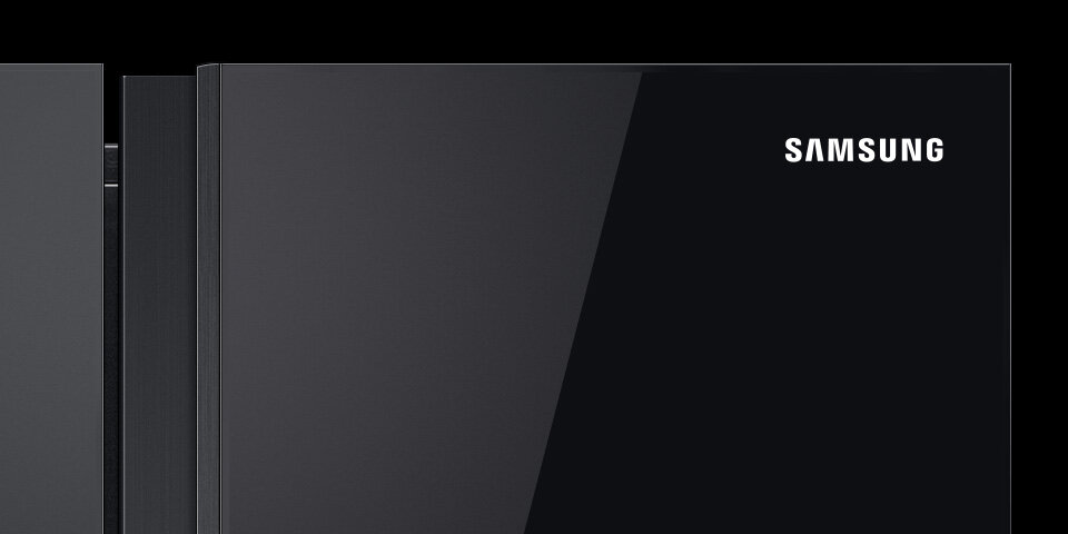 Czarna powierzchnia lodówki z widocznym logo \'SAMSUNG\' w prawym górnym rogu. Powierzchnia jest gładka i błyszcząca.