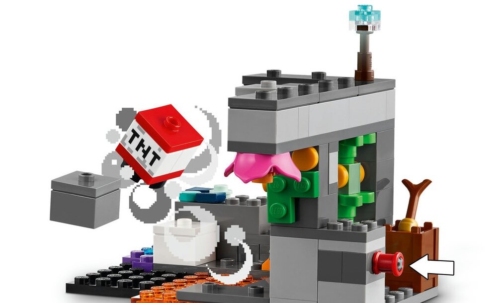 Zestaw klocków LEGO przedstawiający konstrukcję z szarych i kolorowych elementów, z widocznym czerwonym klockiem z napisem \'TNT\'. W tle znajduje się brązowy element przypominający skrzynię z rośliną.