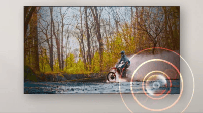 Telewizor wyświetla obraz motocyklisty jadącego przez wodę w lesie. Na ekranie widoczne są koncentryczne kręgi sugerujące efekt dźwiękowy.