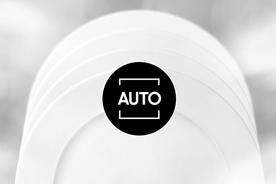Na obrazie widoczne są białe talerze ułożone jeden za drugim. Na środku znajduje się czarne koło z białym napisem \'AUTO\'.