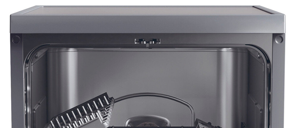 Wnętrze zmywarki w kolorze srebrnym z widocznymi koszami na naczynia i ramieniem spryskującym. Zmywarka ma prosty, nowoczesny design.